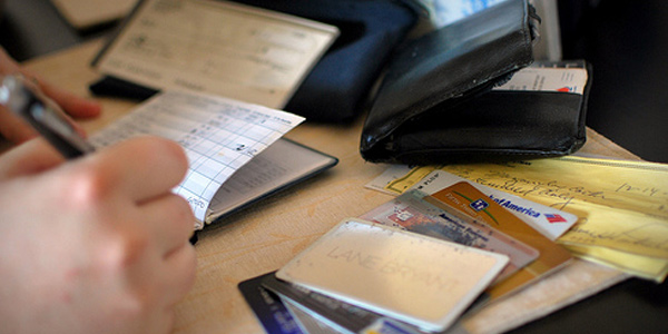 Man writes in notebook beside thick wallet, several credit cards, and a cheque