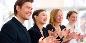Caucasian man and 3 women in business attire smiling and applauding