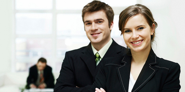 Young Caucasian male and female in business attire smiling at the camera in an office