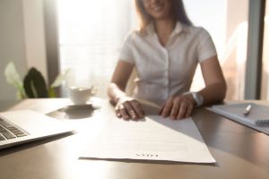 Young woman in white business top sliding a loan agreement across an office table