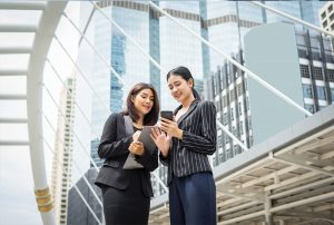 2 young women in office attire looking at a phone screen outside an office building