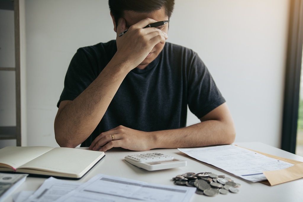 Distressed man with bills and calculator on the table worried about being unable to repay his personal loan and other debts