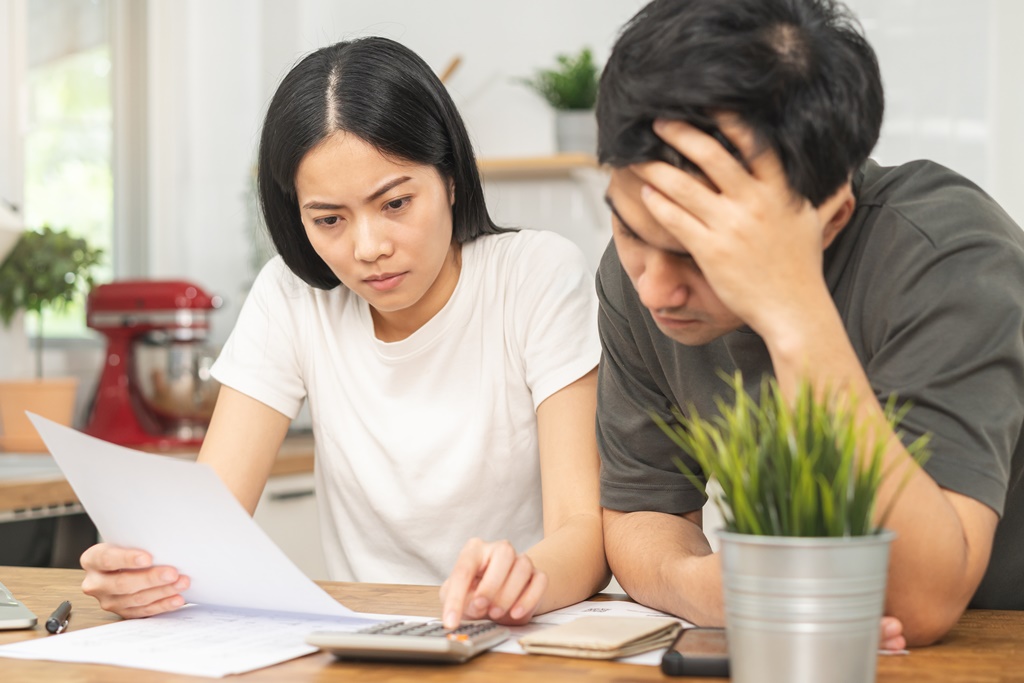 Stressed young couple calculating various debts, wondering if others can take a legal loan in Singapore on their behalf